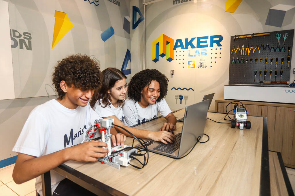 três adolescentes em aula de robótica no laboratório maker, de frente para um notebook