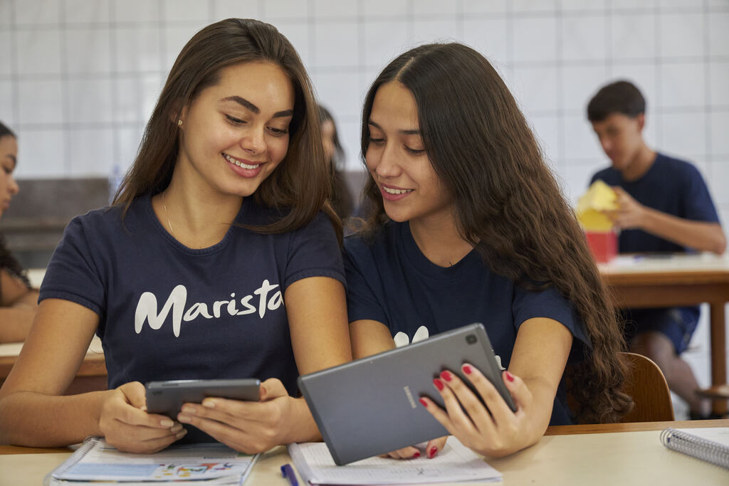 Duas meninas estudantes maristas do Ensino Médio, durante a aula, estudando com a ajuda de seus tablets