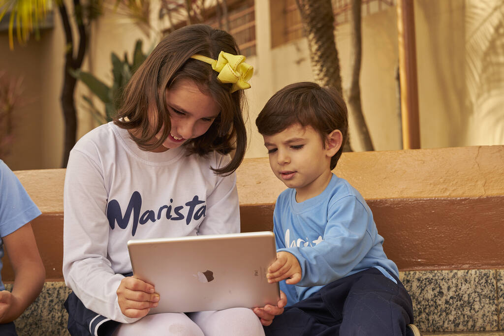 Menino e menina com tablet na mão, na escola. Um exemplo de tecnologia na educação. 